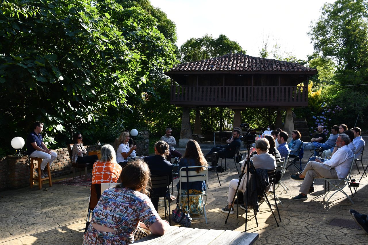 An audience sits beneath trees for an outdoor talk at Diáspora