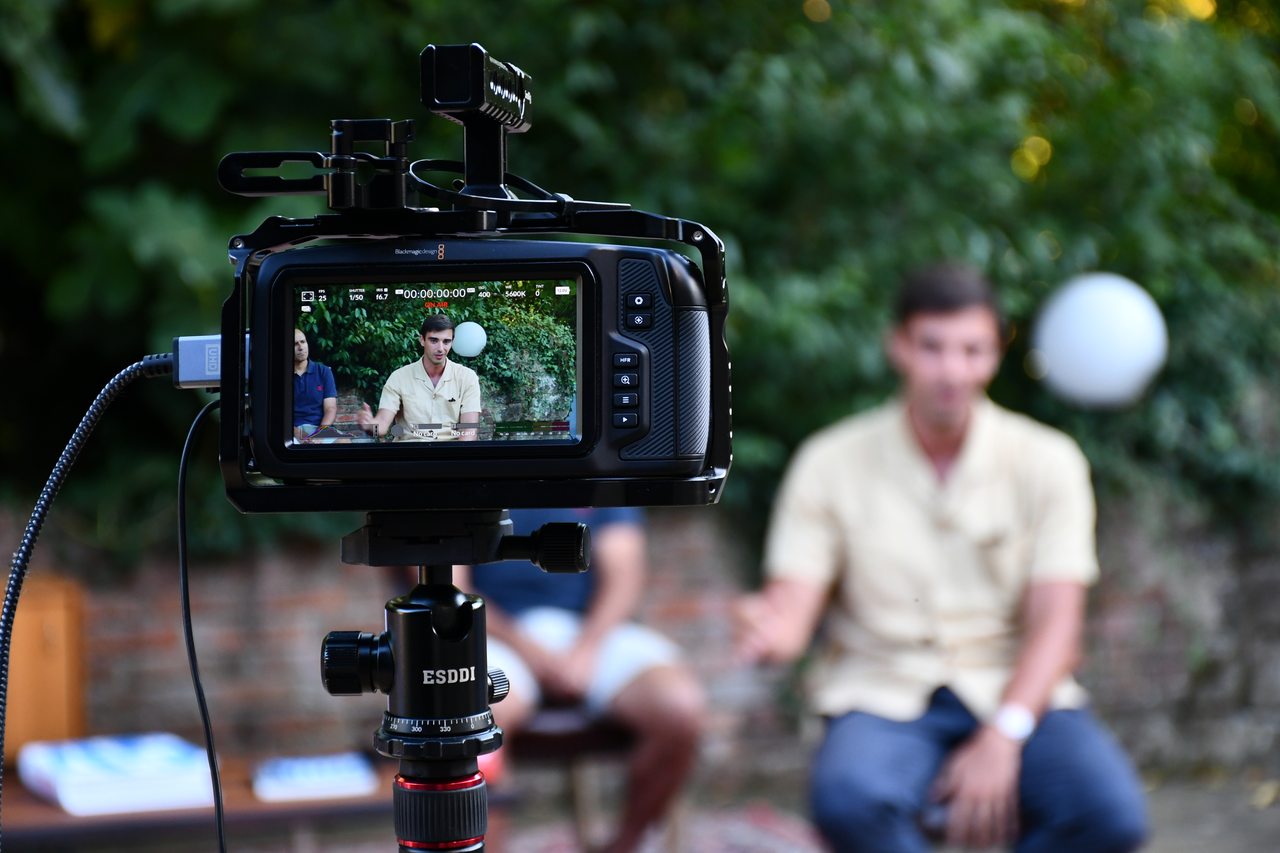 A camera records a seated speaker during an outdoor talk at Diáspora