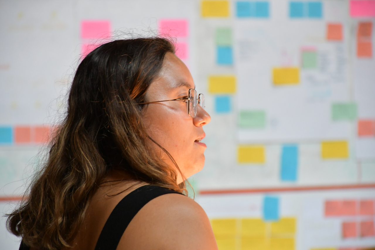 A workshop participant stands beside a wall of colourful notes at Diáspora