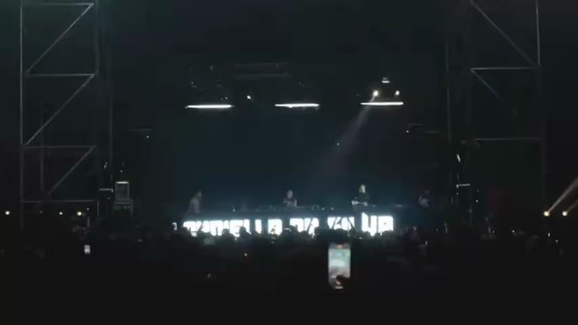A distant nighttime audience facing a live electronic music stage.