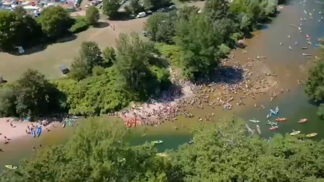 Aerial view of a large outdoor festival gathering beside water and green landscape.